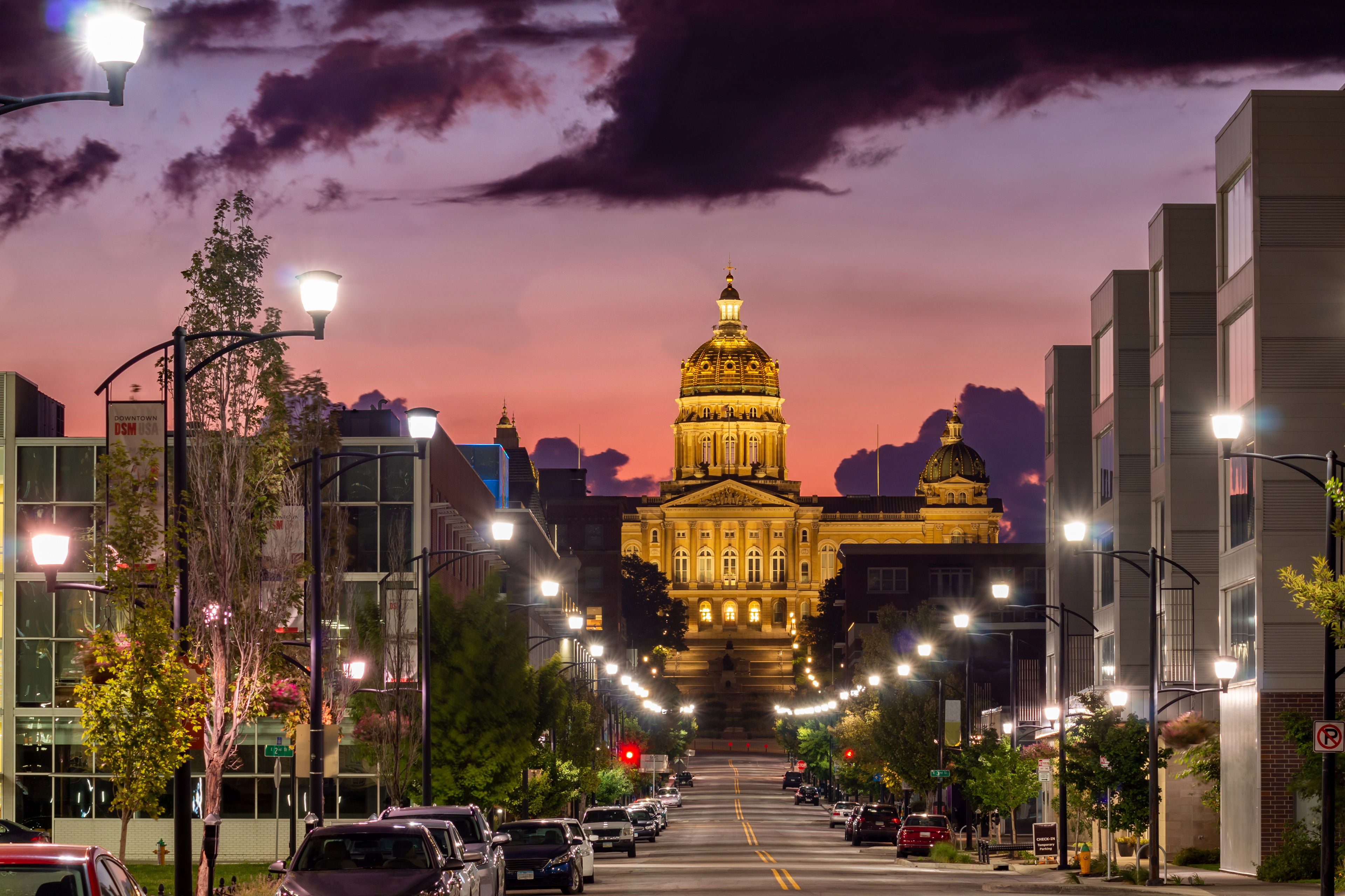 The illuminated Iowa State Capitol at sunrise, seen along a downtown Des Moines street